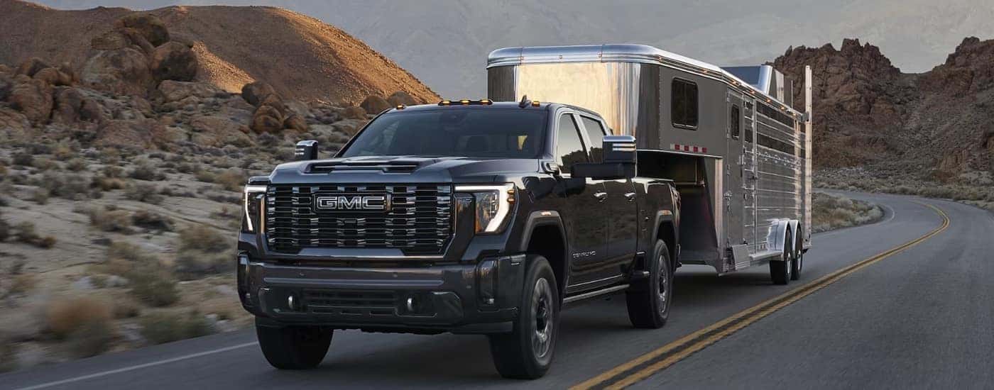 A black 2024 GMC Sierra HD Denali towing a trailer on the highway.