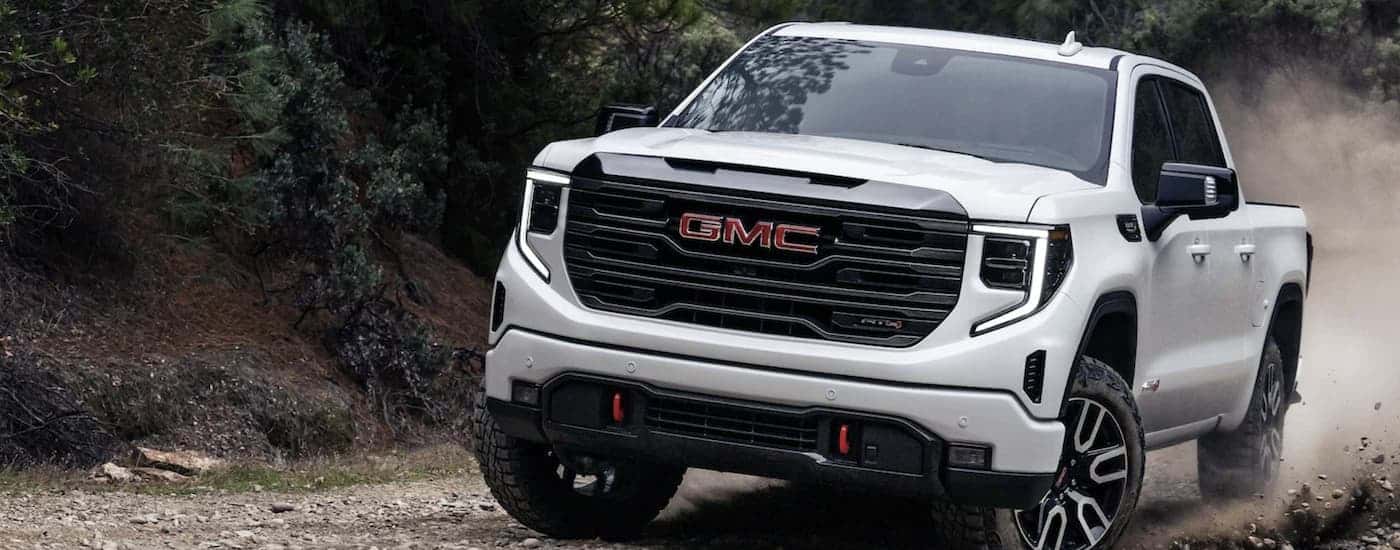 A white 2024 GMC Sierra 1500 AT4 driving down a dirt road.