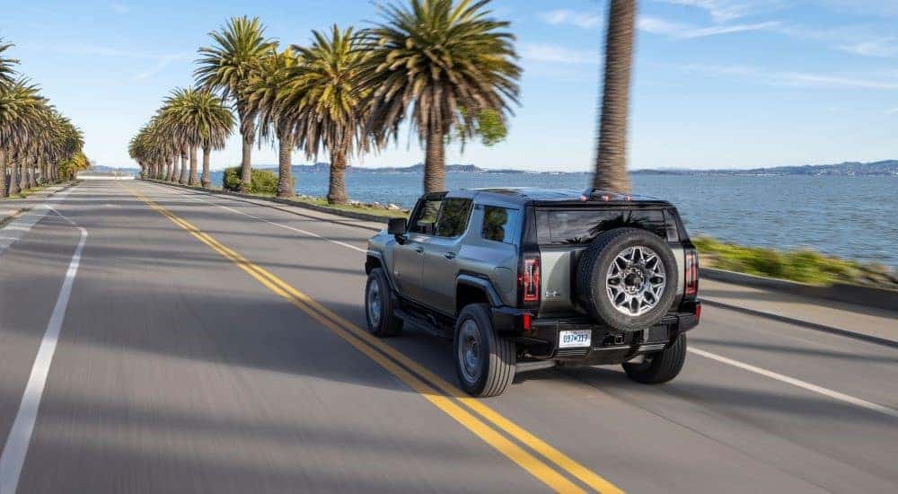 Rear angle view of a grey 2024 GMC Hummer EV SUV driving down a beach road.