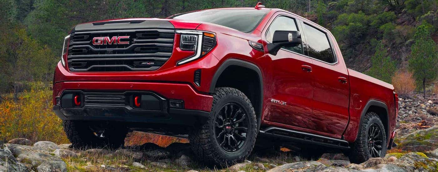 A red 2024 GMC Sierra 1500 AT4X driving over rocky terrain.