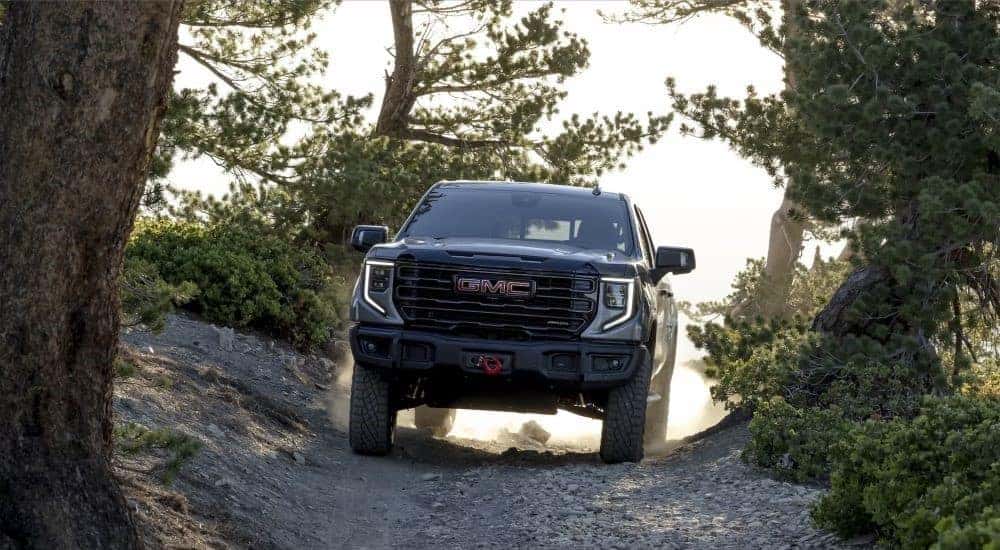 Front view of a grey 2024 GMC Sierra 1500 AT4X AEV driving on a trail in the woods.