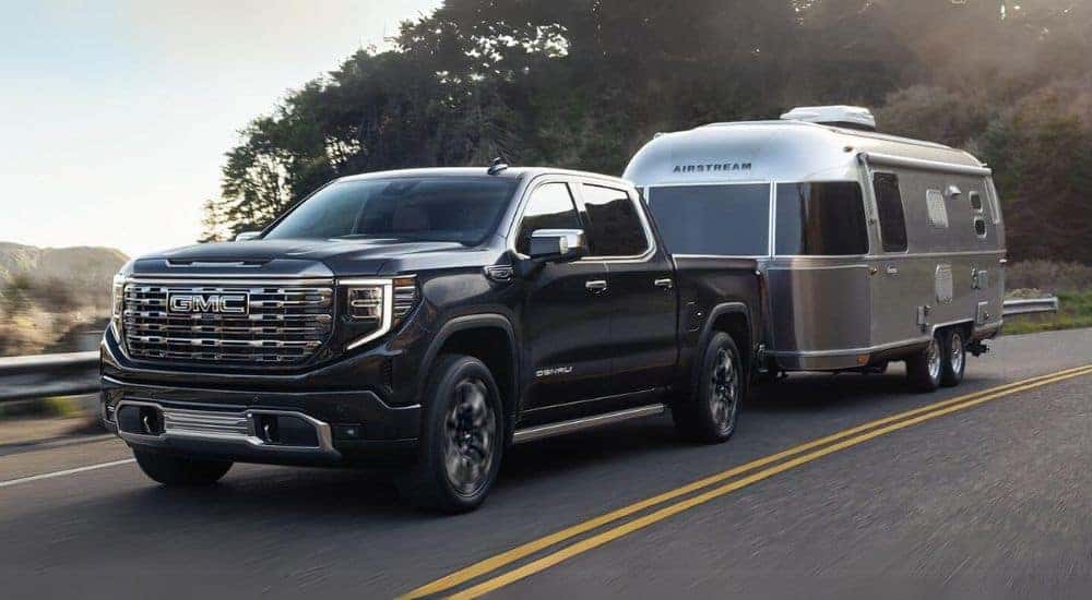 A black 2024 GMC Sierra 1500 Denali towing a trailer down a road.