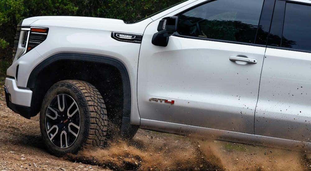 A white 2023 GMC Sierra 1500 AT4 is shown driving off-road.
