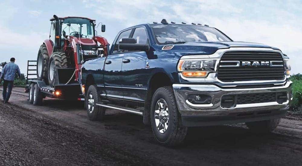A blue 2021 Ram 2500 towing a plow over a dirt road.