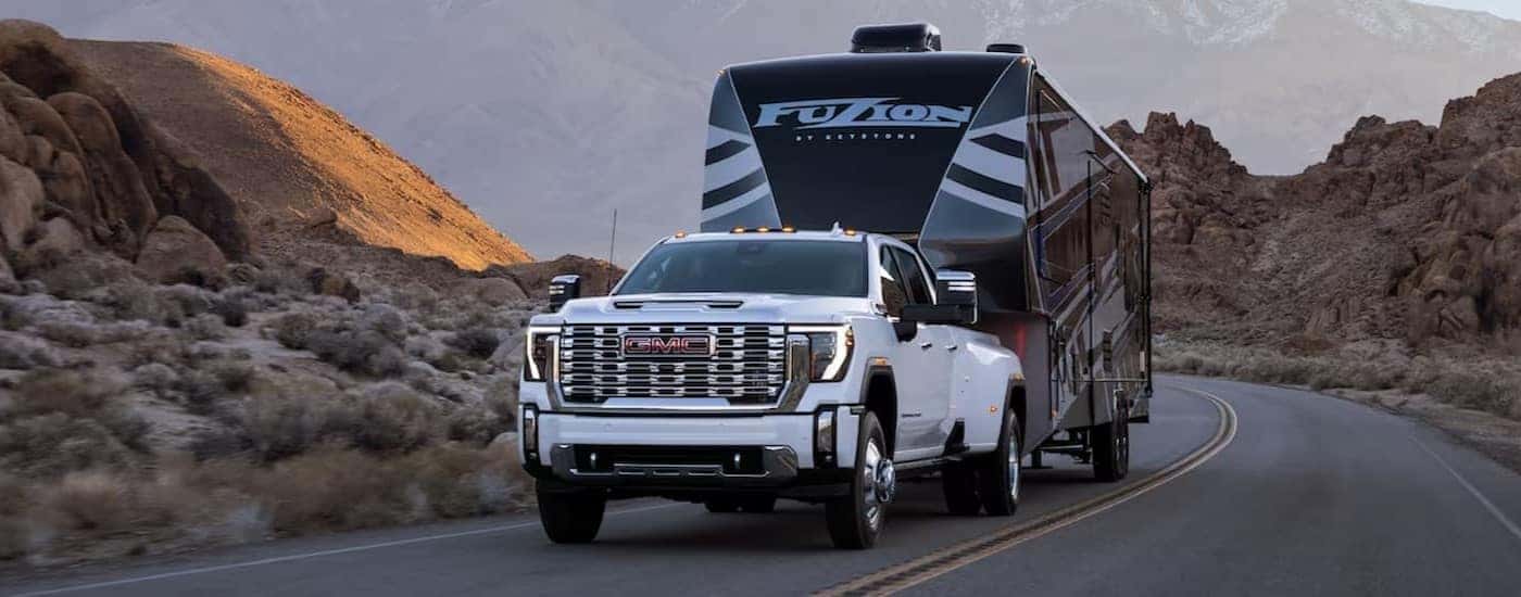 A white 2024 GMC Sierra 2500 Denali is shown towing a trailer after viewing a GMC Sierra 2500 for sale.