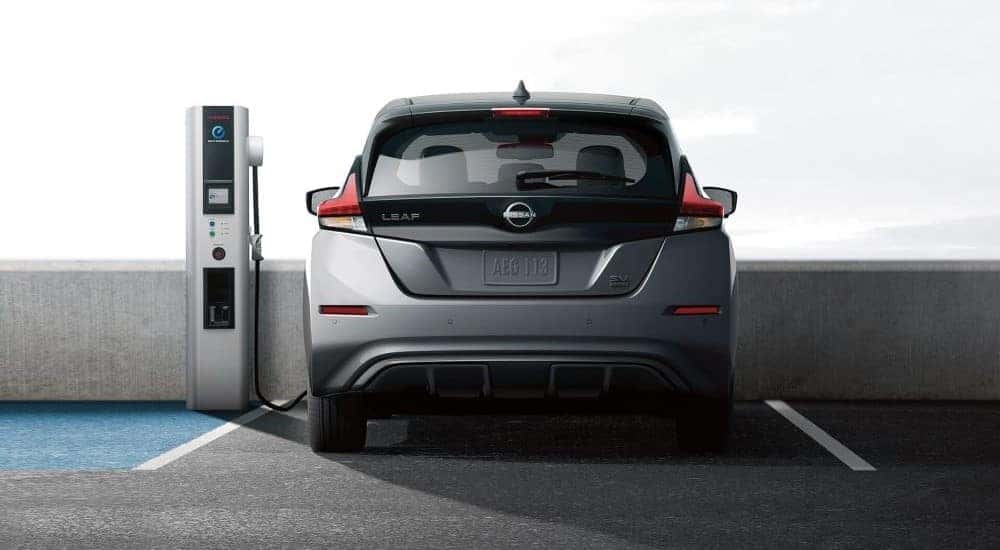 Rear view of a grey 2024 Nissan LEAF plugged in at a public charging station.