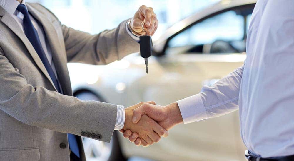 Car salesman shaking a man's hand and offering him a key fob.