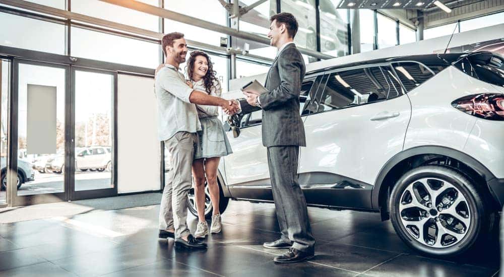 A couple talking to a car salesman at a used car dealer.
