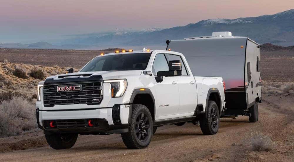A white 2025 GMC Sierra 2500 AT4 is shown towing a trailer off-road.