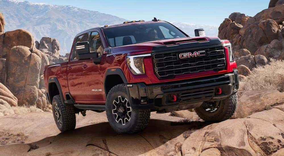 A red 2025 GMC Sierra AT4X is shown parked on a rocky incline.