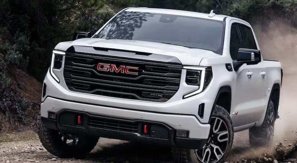 A white 2024 GMC Sierra 1500 AT4X is shown driving off-road.