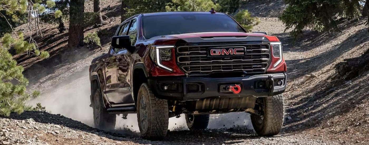 A red 2025 GMC Sierra 1500 AT4X is shown driving on a rocky path.