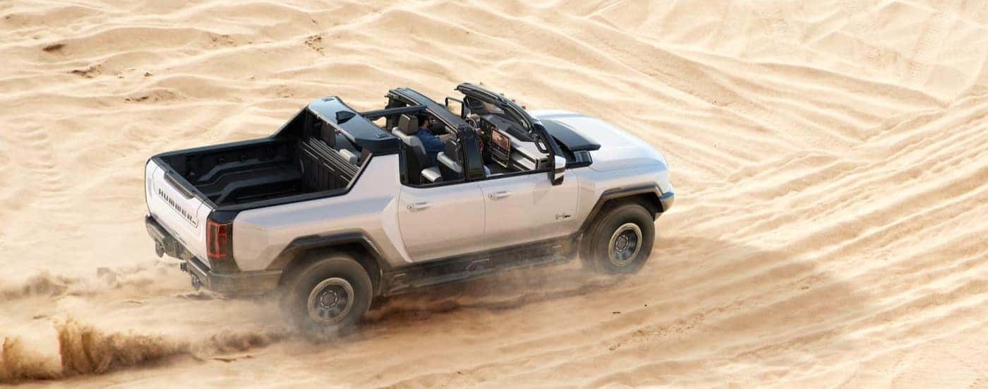 A white 2024 GMC Hummer EV pickup is shown driving off-road.