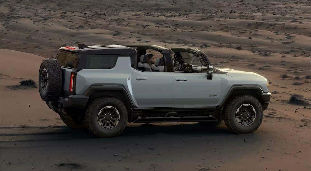 Side right angled view of a white 2025 GMC Hummer EV SUV parked off-road in a desert.