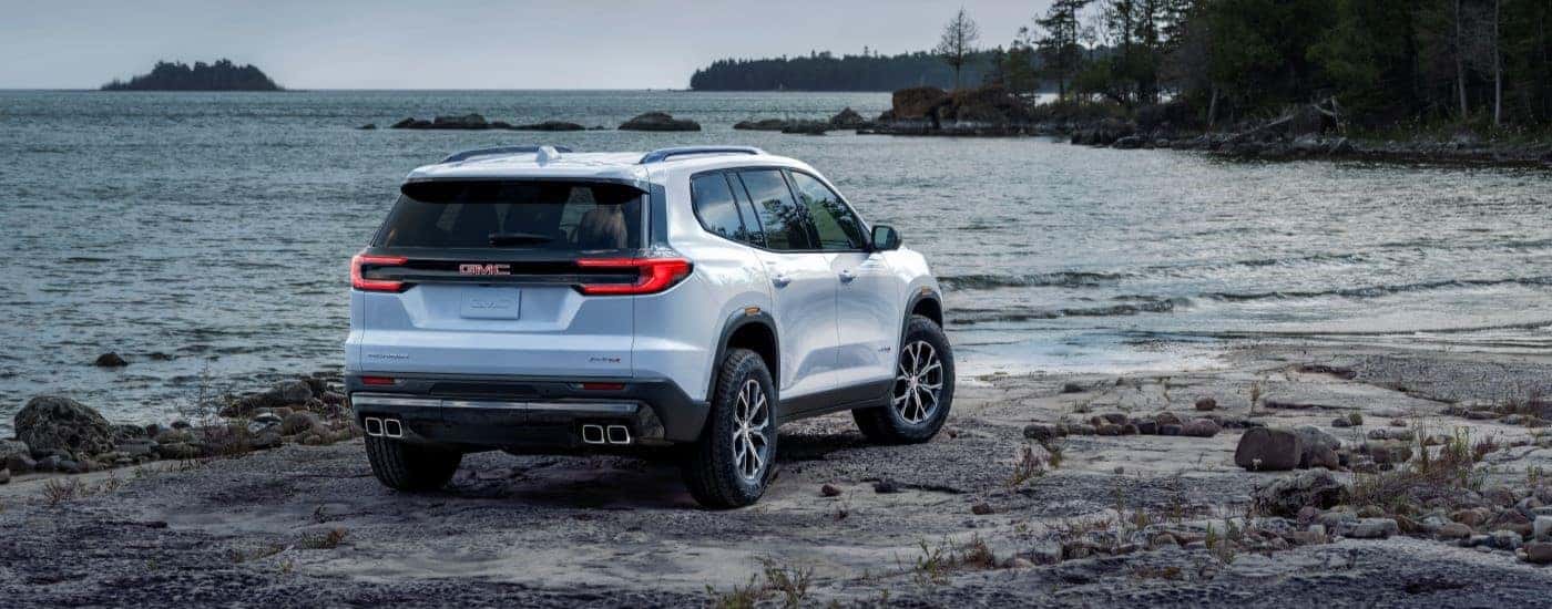 Rear view of a white 2024 GMC Acadia AT4 parked on a beach after visiting a GMC dealer near Alpharetta.