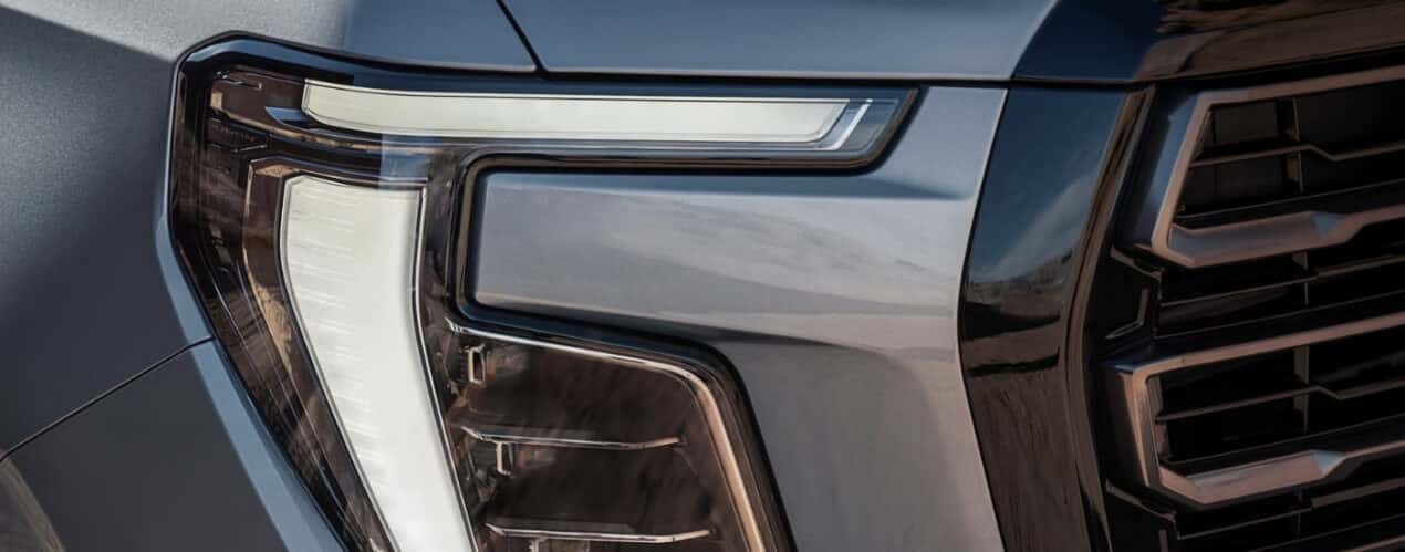 A close-up shows the passenger side headlight on a grey 2025 GMC Yukon.
