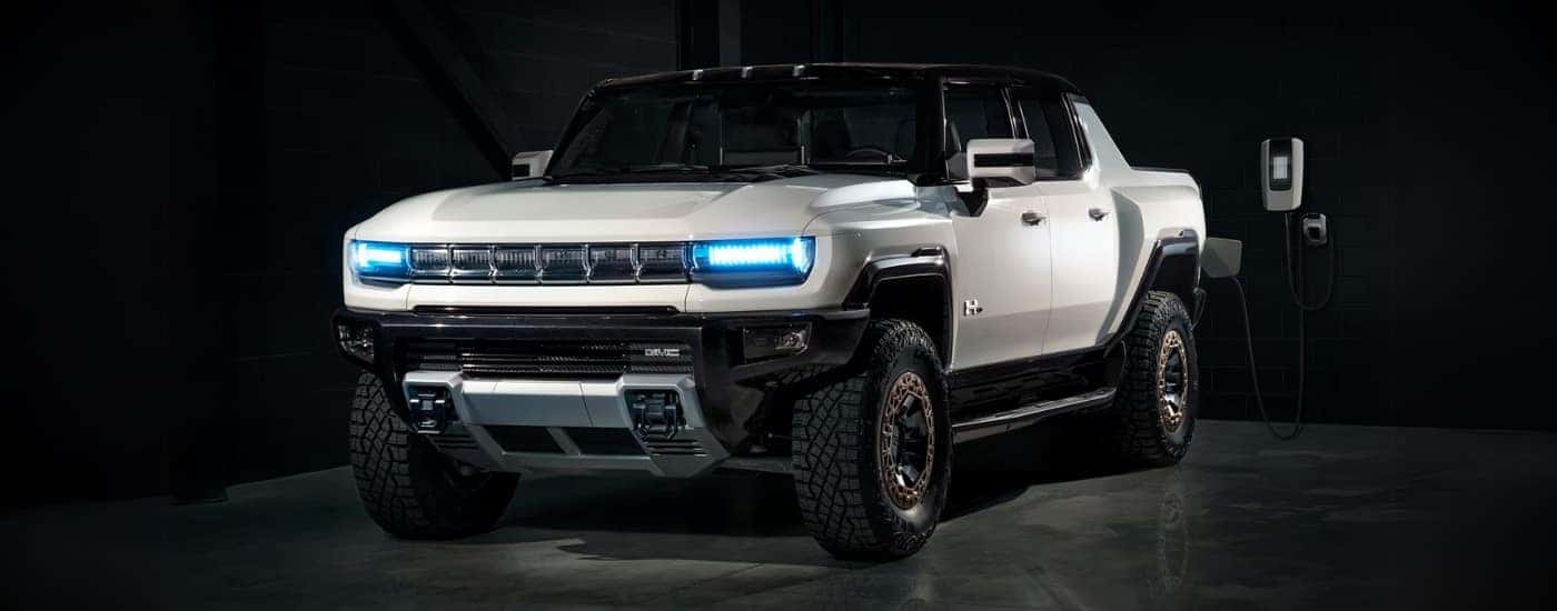 A white 2025 Hummer EV for sale is charging in a garage.