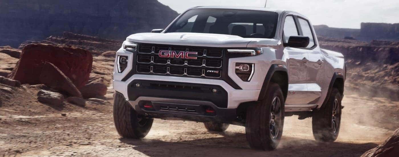 A white 2024 GMC Canyon AT4 off-roading in a dusty area.