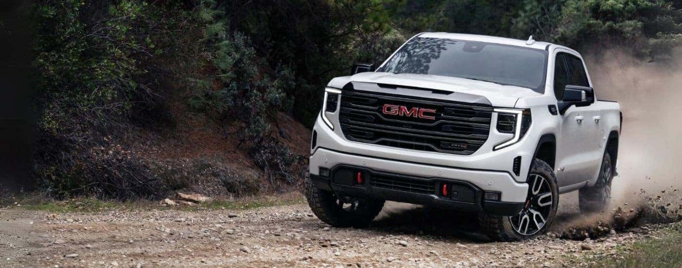 A white 2023 GMC Sierra 1500 for sale is shown driving off-road.