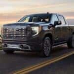 Black 2025 GMC Sierra 1500 Denali for sale driving around a bend.