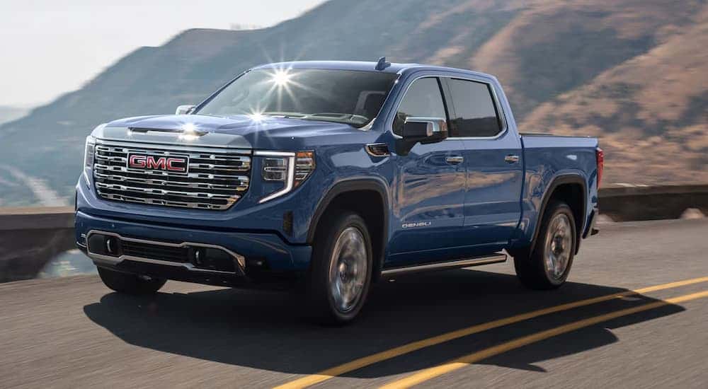 Blue 2025 GMC Sierra 1500 Denali driving down a road.