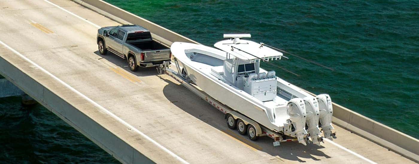 A grey 2025 GMC Sierra 2500 HD Denali towing a boat over a bridge.