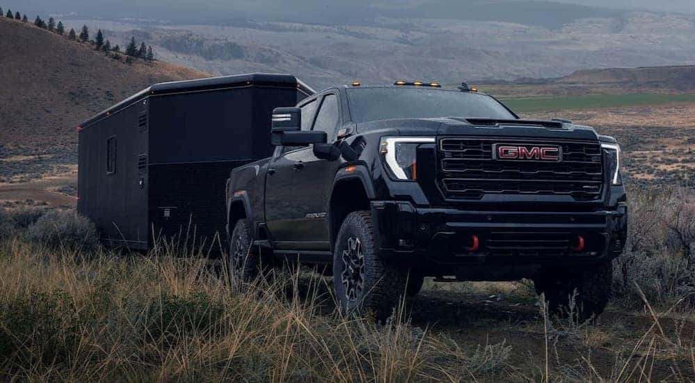 A black 2026 GMC Sierra 2500 HD towing a trailer off-road.