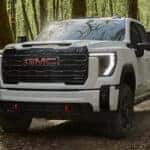 White 2026 GMC Sierra 3500 HD AT4 driving on a woodland trail