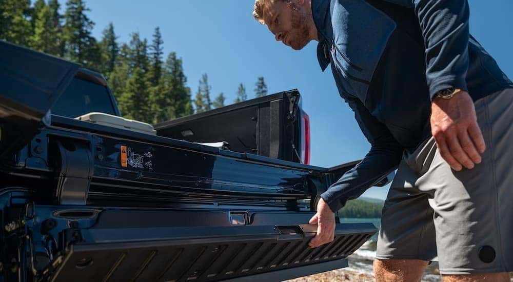 A person opening the tailgate of a black 2026 GMC Sierra 1500.