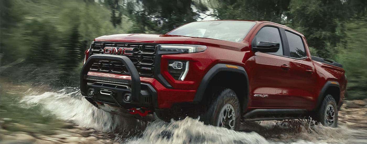 A red 2026 GMC Canyon AT4X off-roading in water