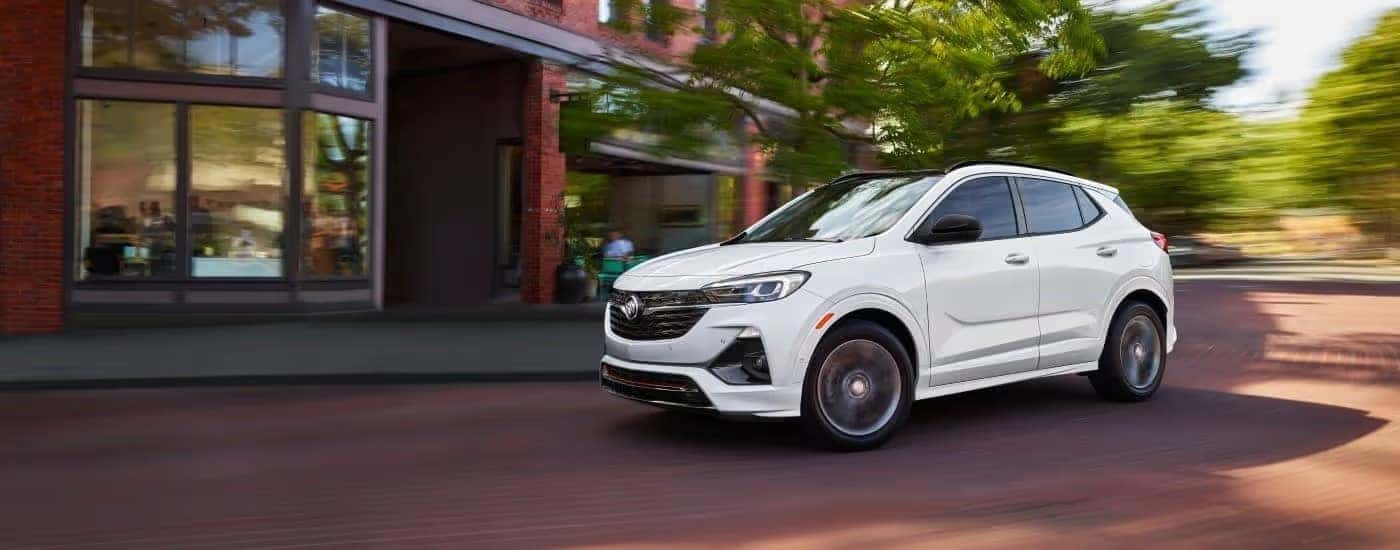 A white 2023 Buick Encore GX is shown driving past a shop.