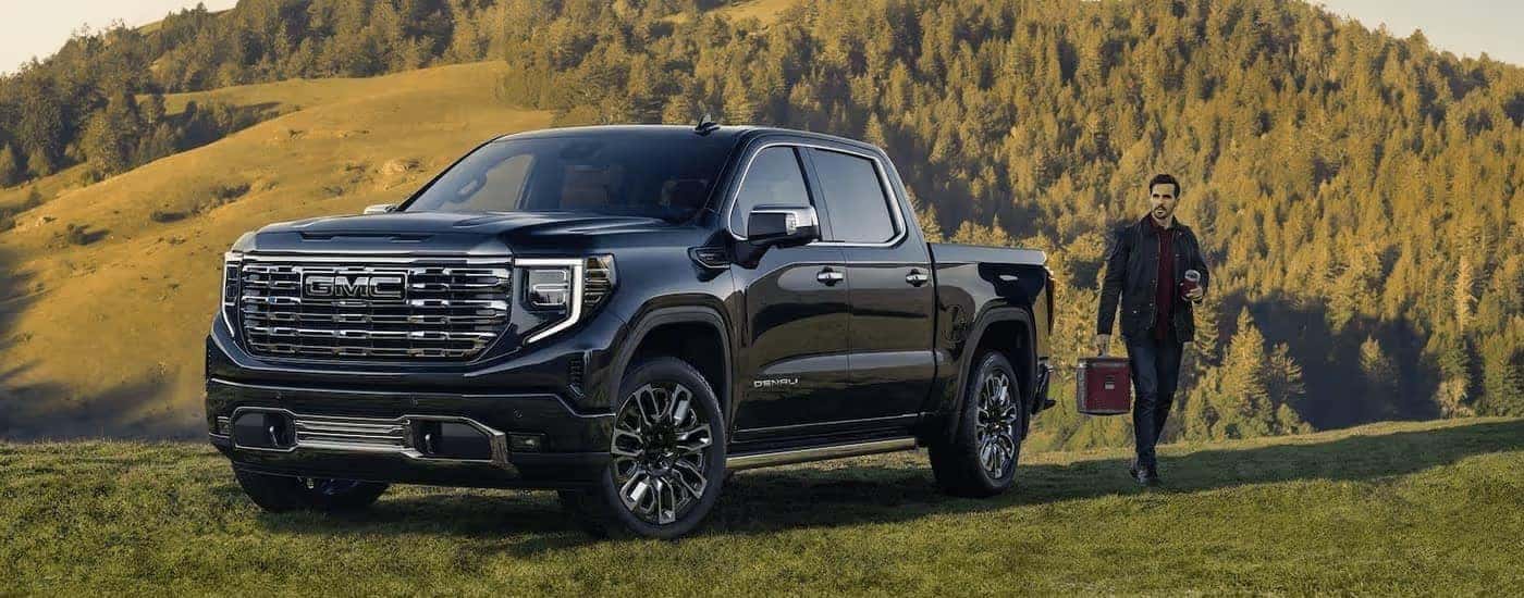 A black 2023 GMC Sierra 1500 Denali is shown parked on a grassy area overlooking a hill.