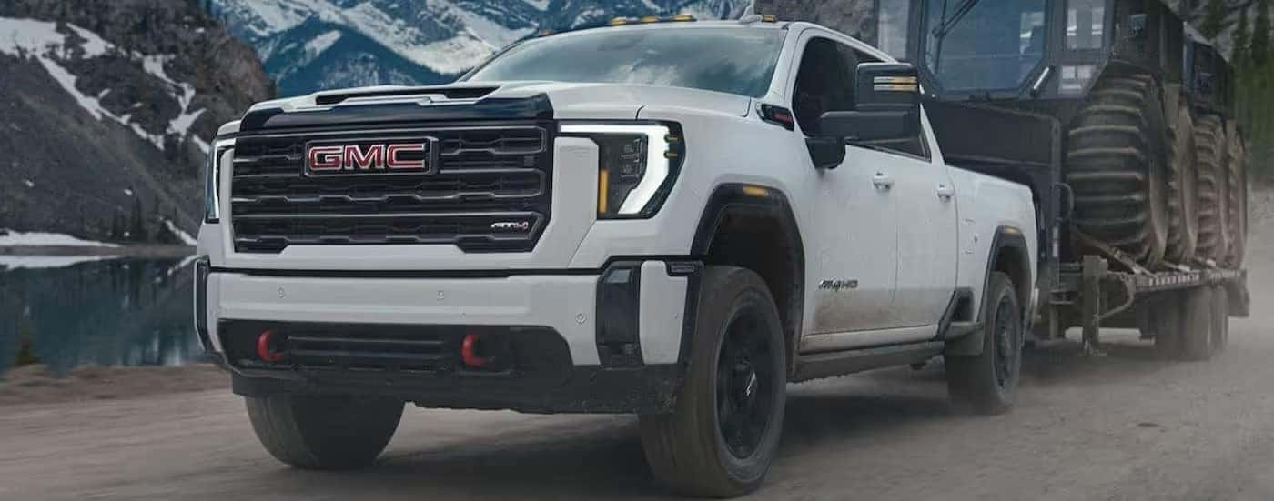 A white 2024 GMC Sierra 3500 HD AT4 is shown towing a trailer.