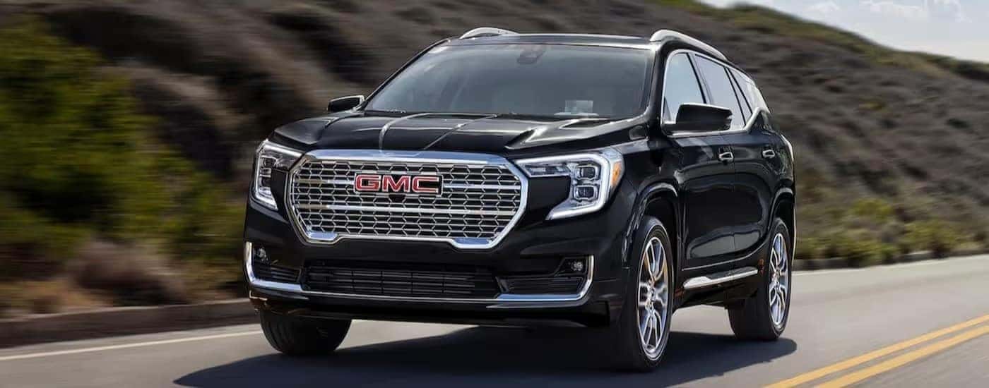 A black 2024 GMC Terrain is shown driving on a highway.