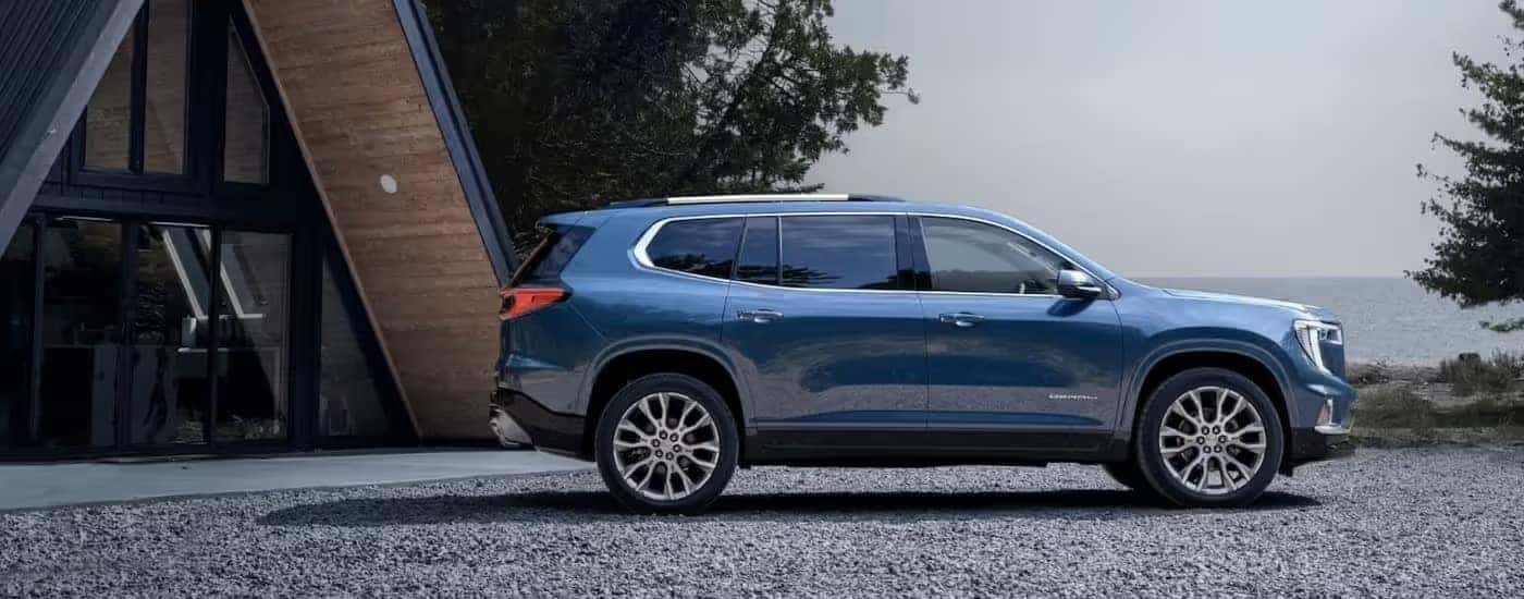 A blue 2025 GMC Acadia Denali is parked on gravel driveway.