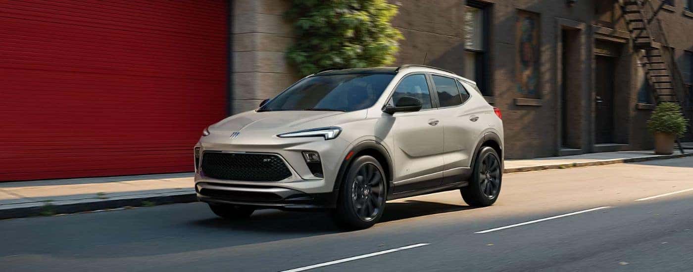 A silver 2026 Buick Encore GX shown driving by a building.