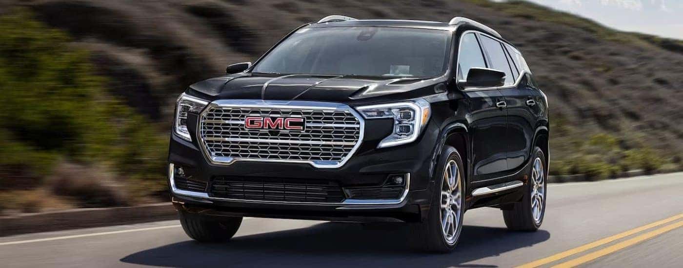 A black 2024 GMC Terrain Denali driving by a grassy hill.