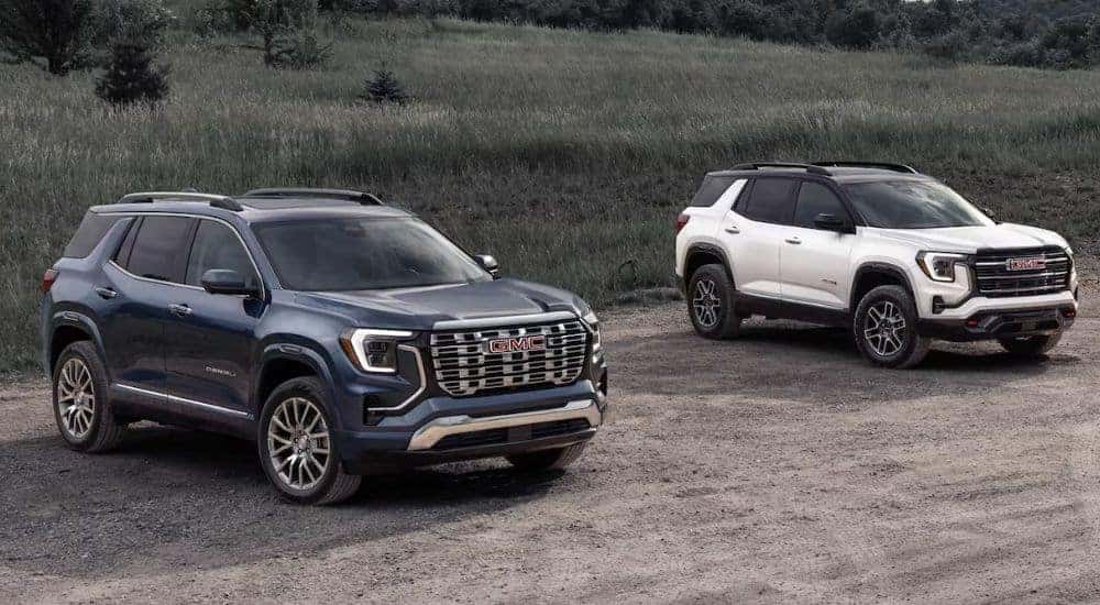 A blue 2026 GMC Terrain Denali and a white 2026 GMC Terrain AT4 parked by a field.