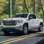 White 2026 Sierra 1500 driving over a sunlit bridge.