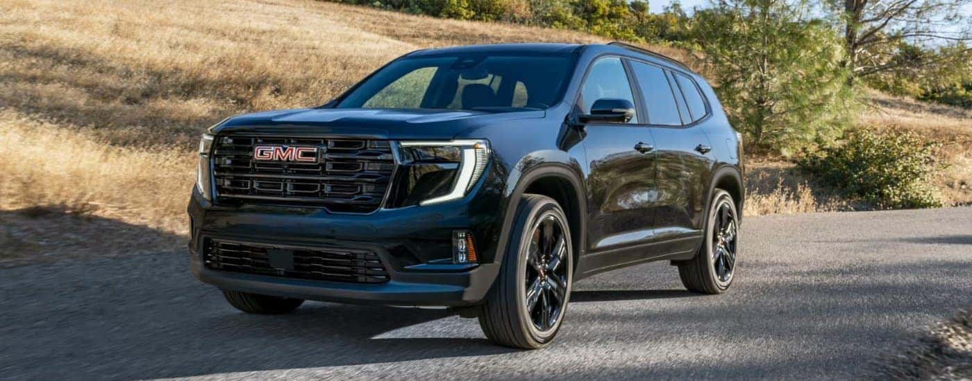 Black 2026 GMC Acadia Elevation driving up an open road