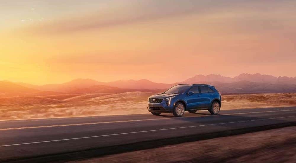A blue 2023 Cadillac XT4 is shown driving at sunset.