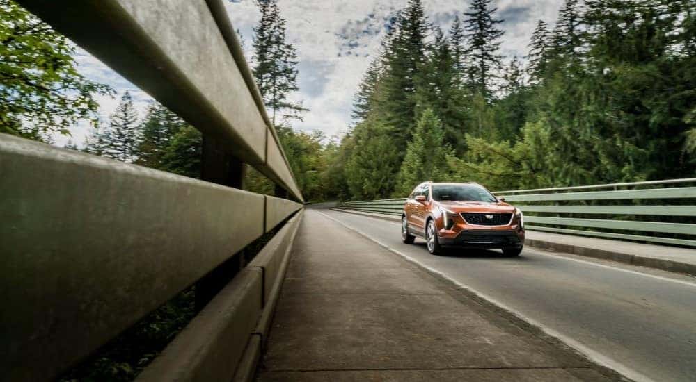 An orange 2019 Cadillac XT4 is shown driving over a bridge.