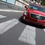 A red 2015 Cadillac ATS is shown driving over a crosswalk after looking for a Certified Pre-owned Cadillac for sale.