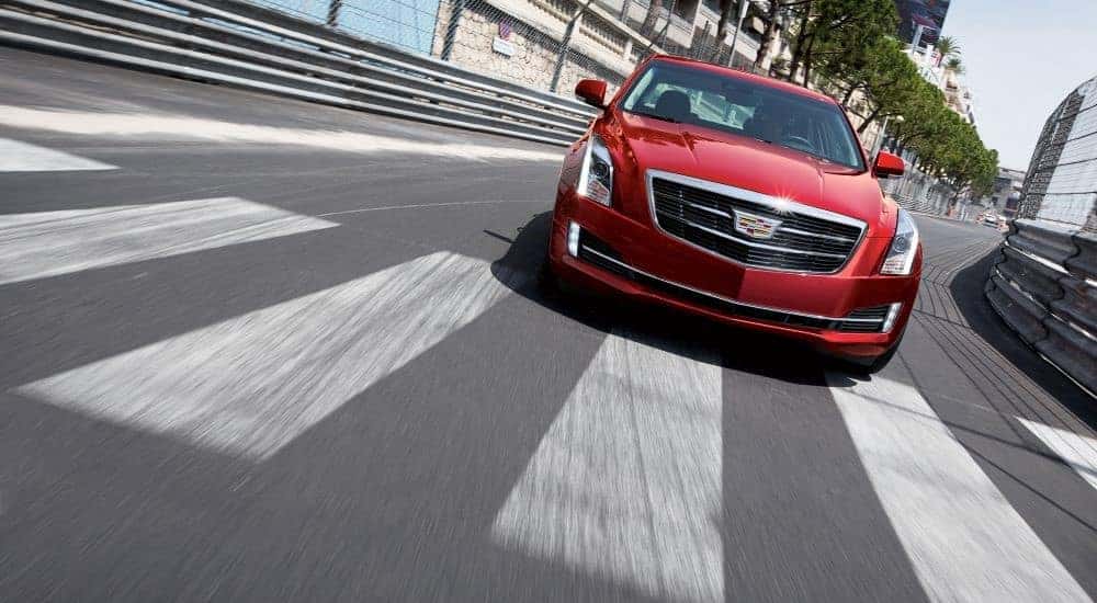 A red 2015 Cadillac ATS is shown driving over a crosswalk after looking for a Certified Pre-owned Cadillac for sale.