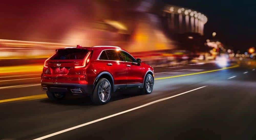 A red 2024 Cadillac XT4 is shown driving on a city street at night.