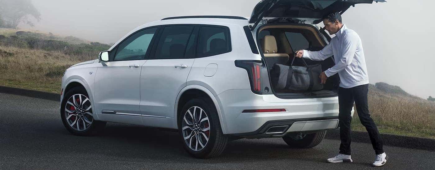 A man is shown unloading cargo from the rear hatch of a white 2024 Cadillac XT6.