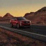 A red 2024 Cadillac XT6 is shown driving on a highway.