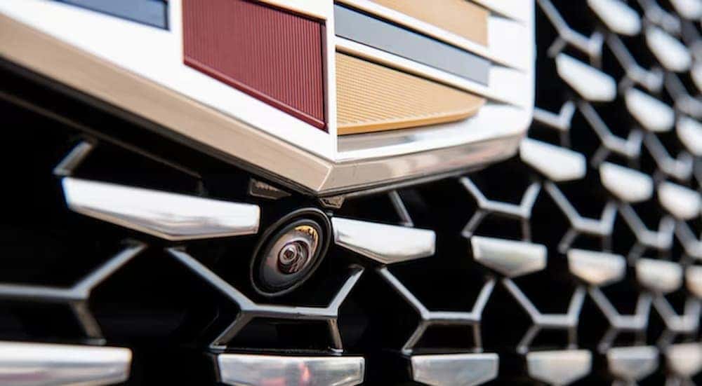 A close-up of a camera on a Cadillac grille is shown.