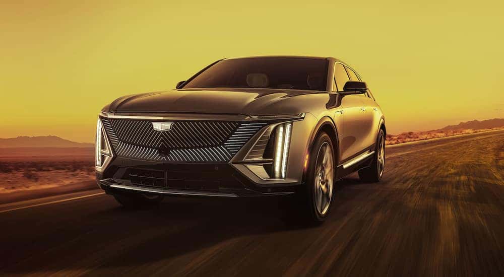 A silver 2024 Cadillac LYRIQ driving on a highway at sunrise.