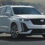 A white 2024 Cadillac XT6 for sale is shown parked near an ocean.